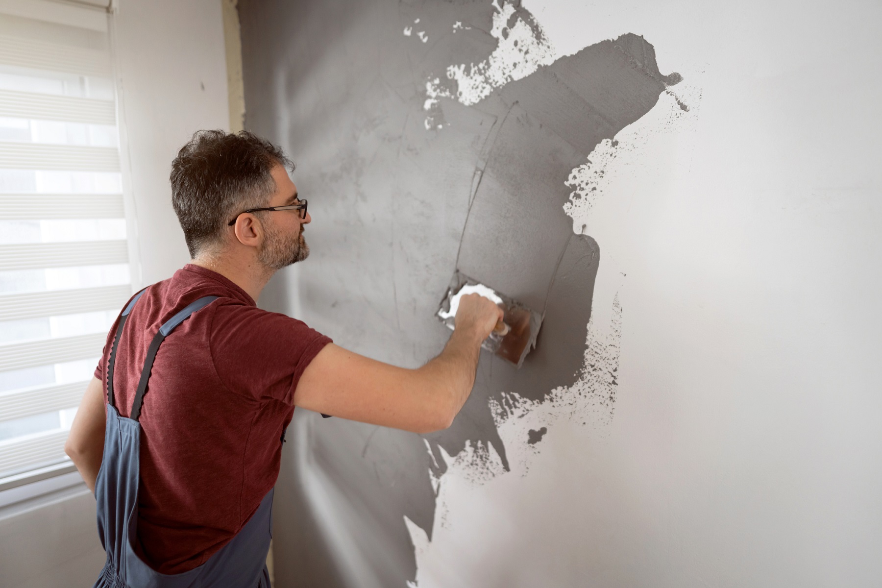 Male Caucasian craftperson, using spatula to coat the wall with plaster