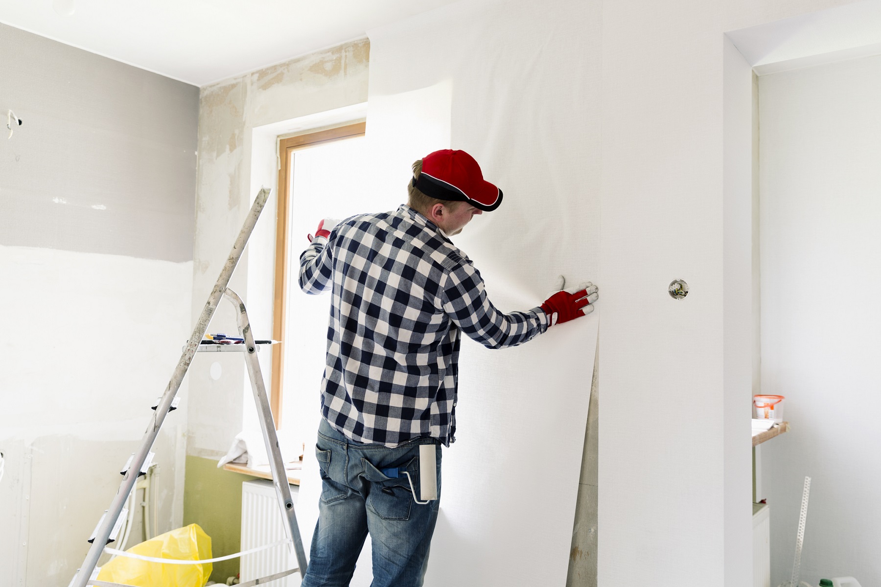 Glueing wallpapers at home. Young man, worker is putting up wallpapers on the wall. Home renovation concept