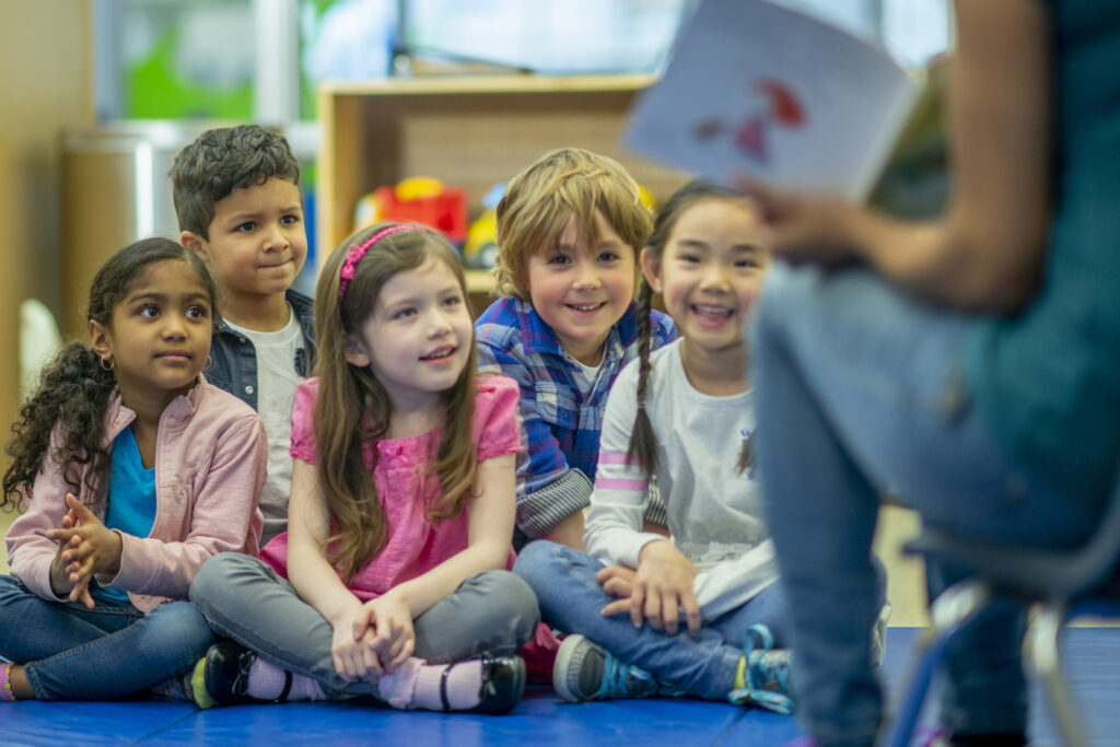 Young children sat together listening to an adult tell a story.