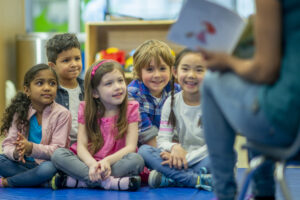 Young children sat together listening to an adult tell a story.