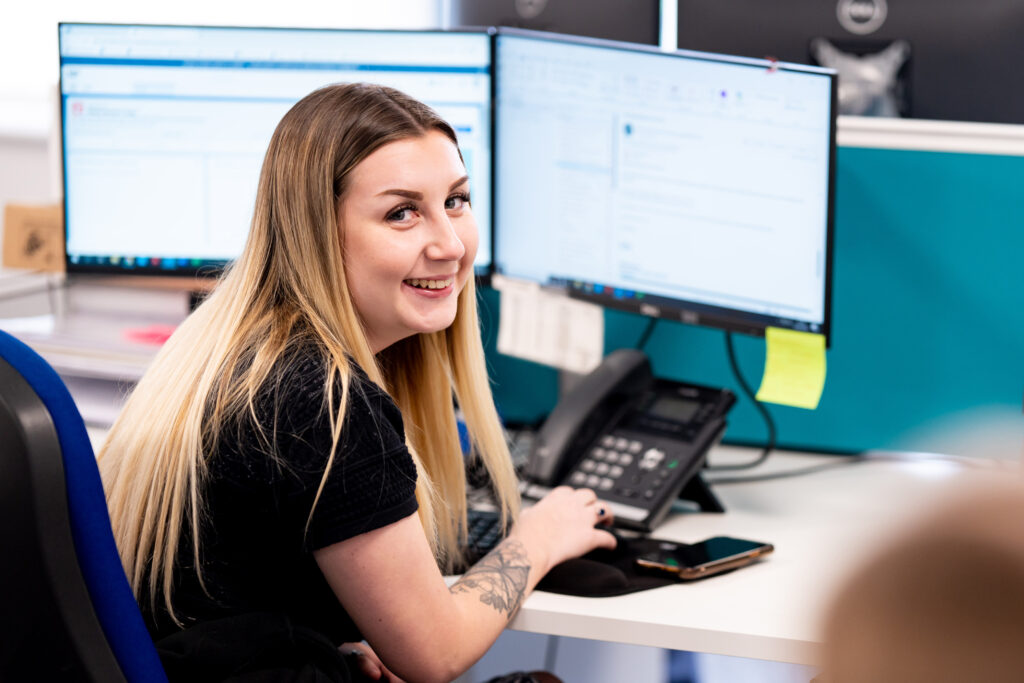 A picture of Elle looking back over her shoulder, sitting at her desk in front of a computer.