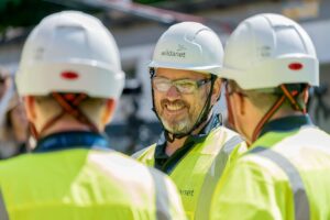 Telecoms Field Operatives in conversation, wearing yellow hi-vis, white hard hats and safety glasses.