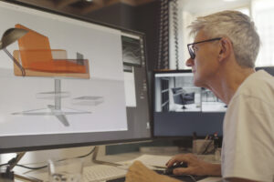 Image of a mature male furniture designer working with CAD to design a contemporary chair, he’s working on a large computer screen.