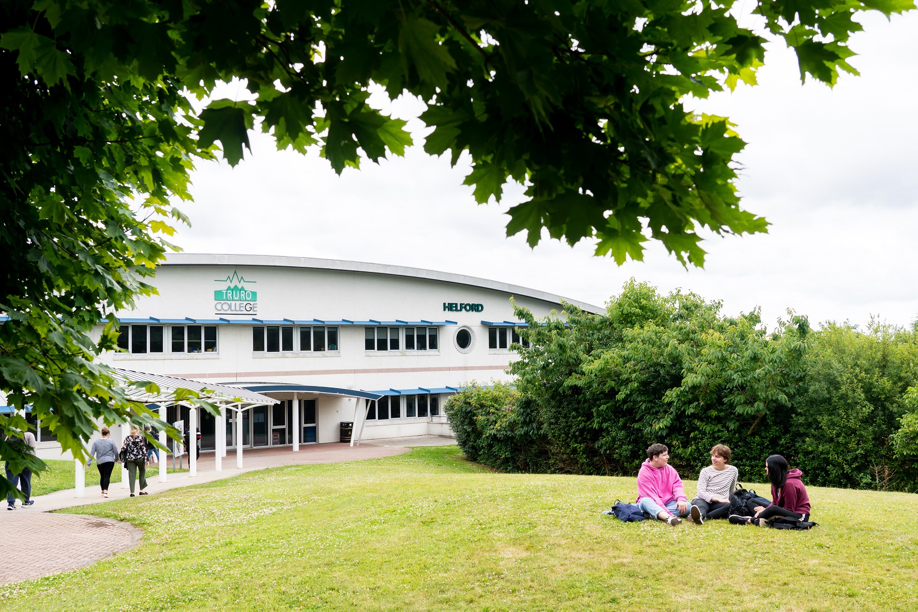 A trio of students sit on the grass outside the Helford building on the Truro campus.