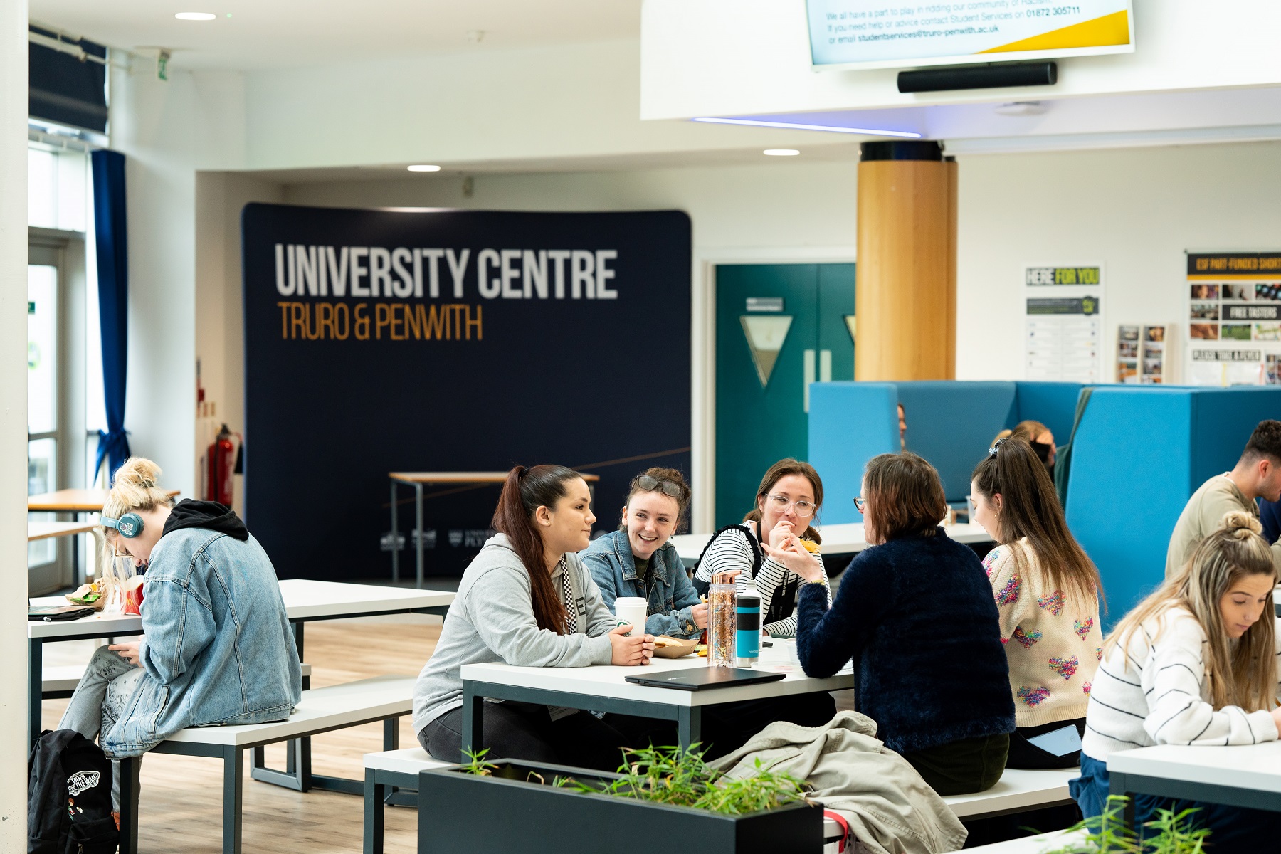 A group of adult students sit at a table in the Fal building chatting and enjoying drinks.