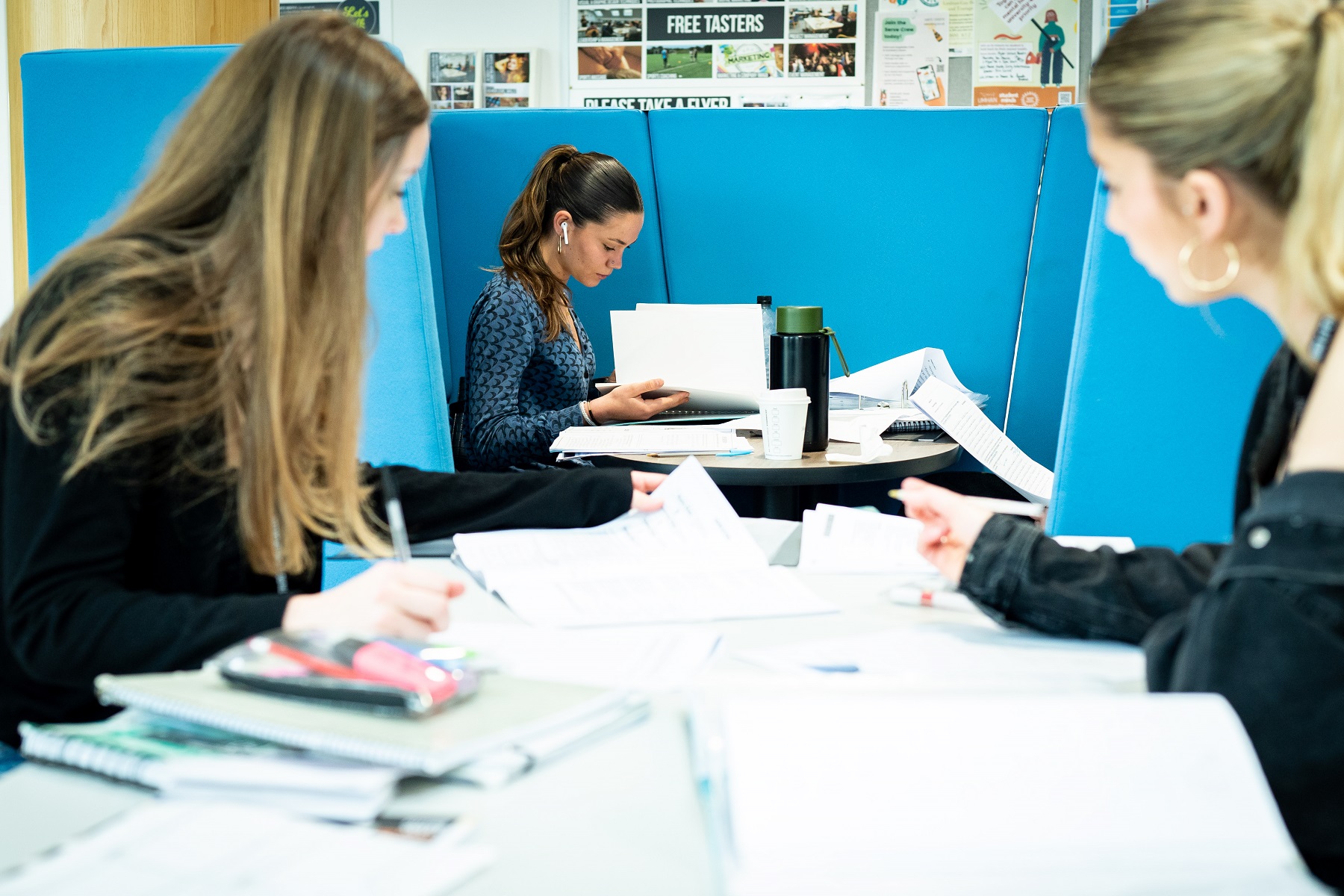 Students sit in the Fal building studying with papers and folders around them.