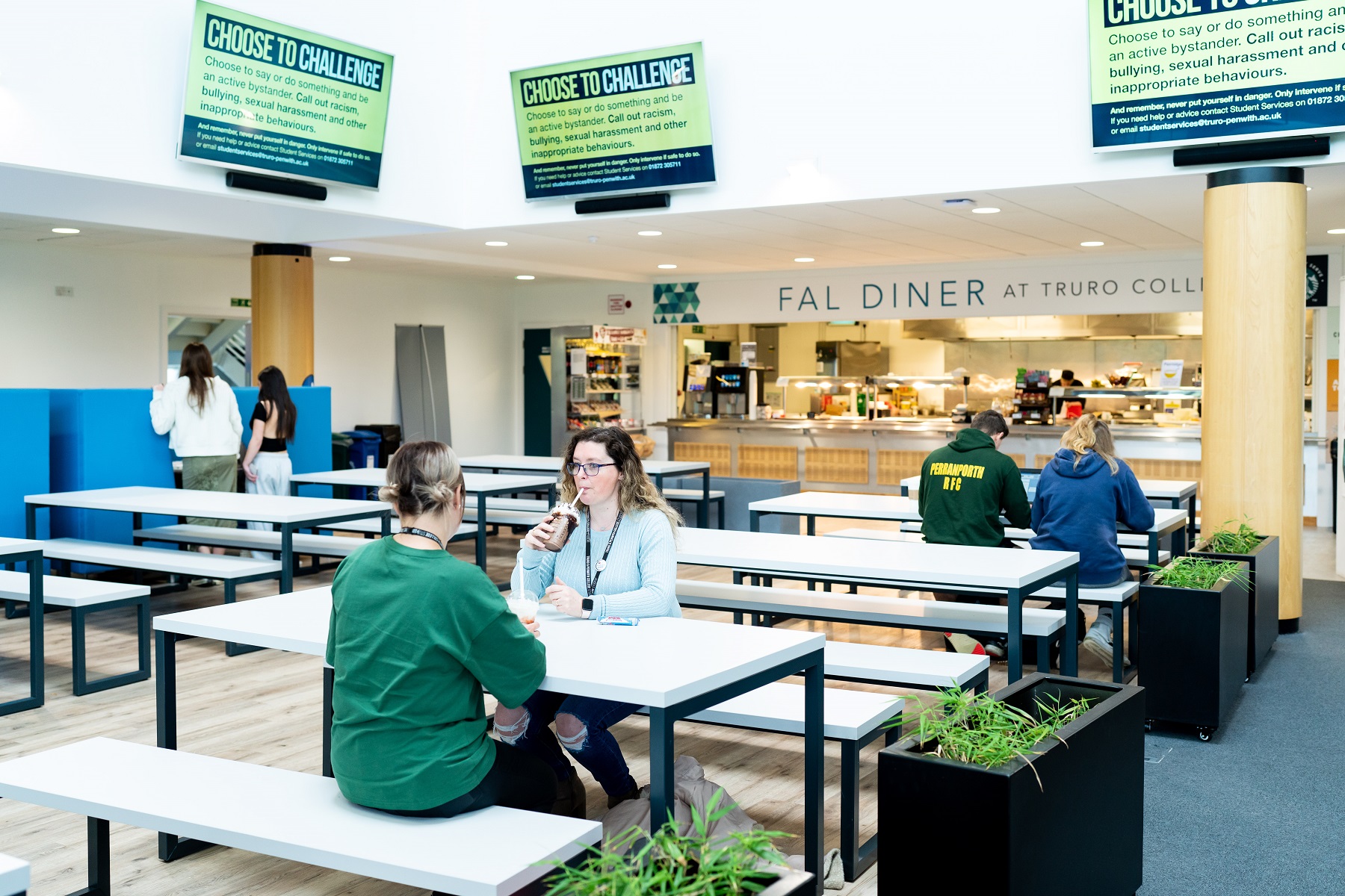 Two students sit at a table in the Fal building canteen enjoying cold drinks.