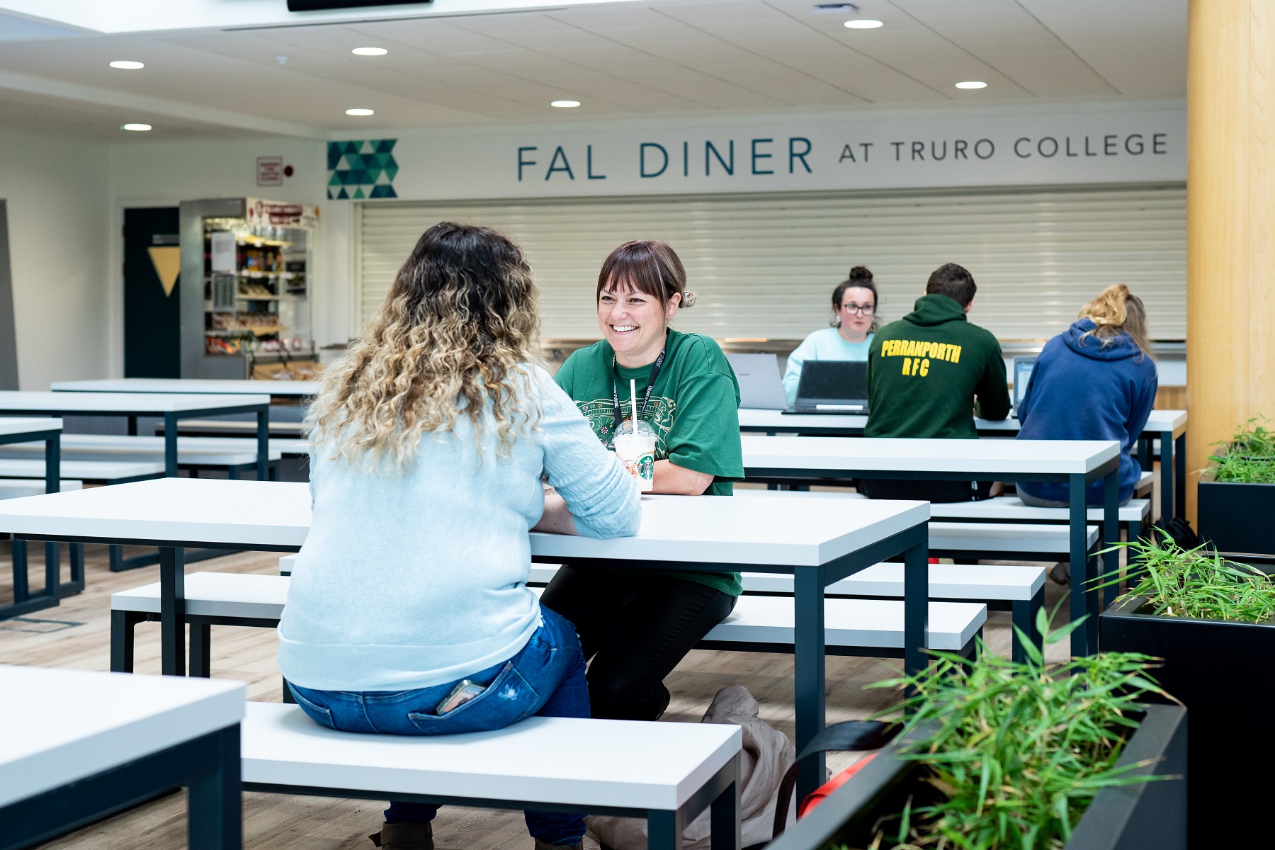 Two adult students sit in the Fal building canteen at the University Centre Truro and Penwith enjoying a starbucks drink and chatting.