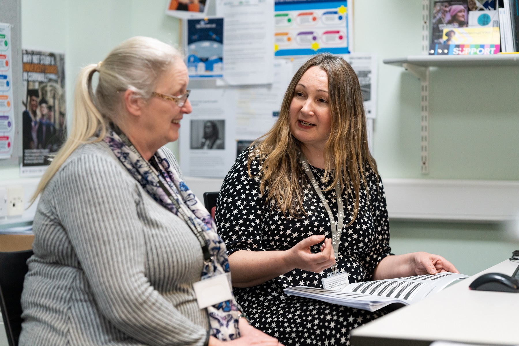 An adult student sits in an office with our Careers and Employability lead looking over some documents.