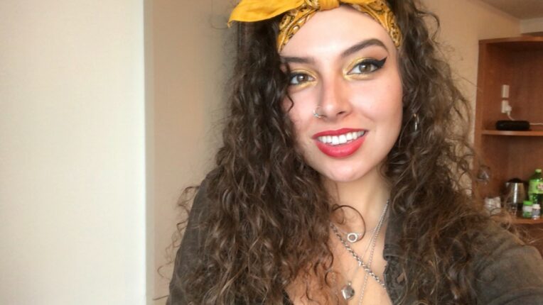 A student with long dark brown curly hair with a yellow headband and red lipstick smiles at the camera.