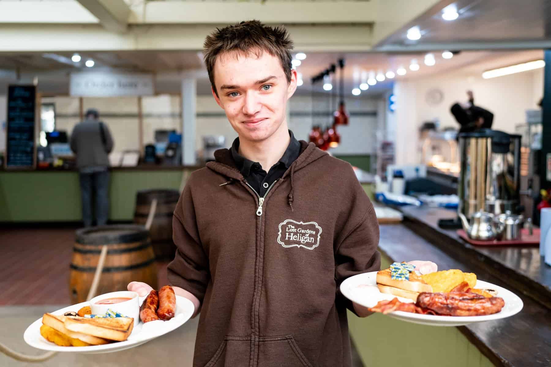 An apprentice working at The Lost Gardens of Heligan looks at the camera holding two plates of breakfast