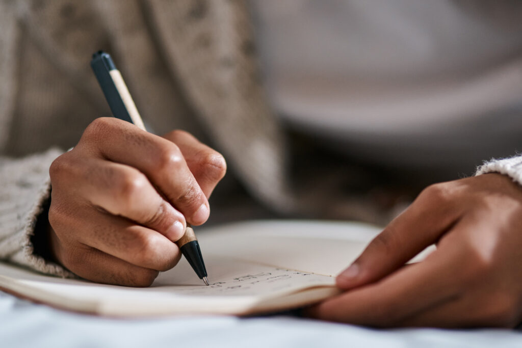 Cropped shot of a man writing in a notebook on his bed at home