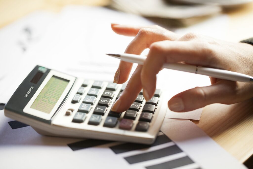 Close up of a manicured hand resting on a calculator and also holding a pen