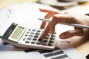 Close up of a manicured hand resting on a calculator and also holding a pen