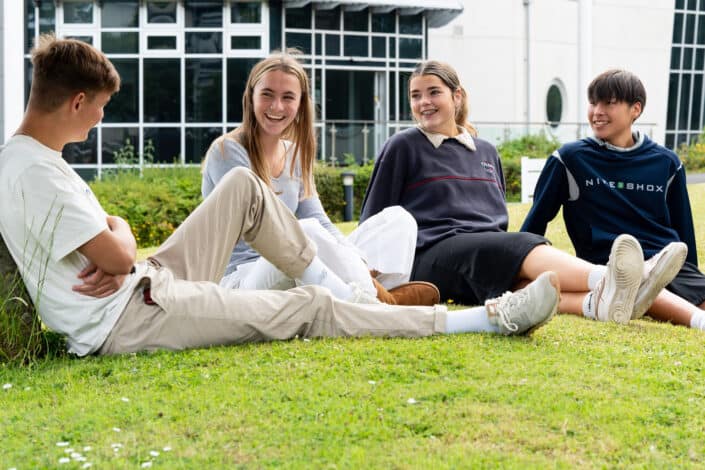 Four students relax on the grass outside one of the buildings at Penwith campus, all smiling and chatting.