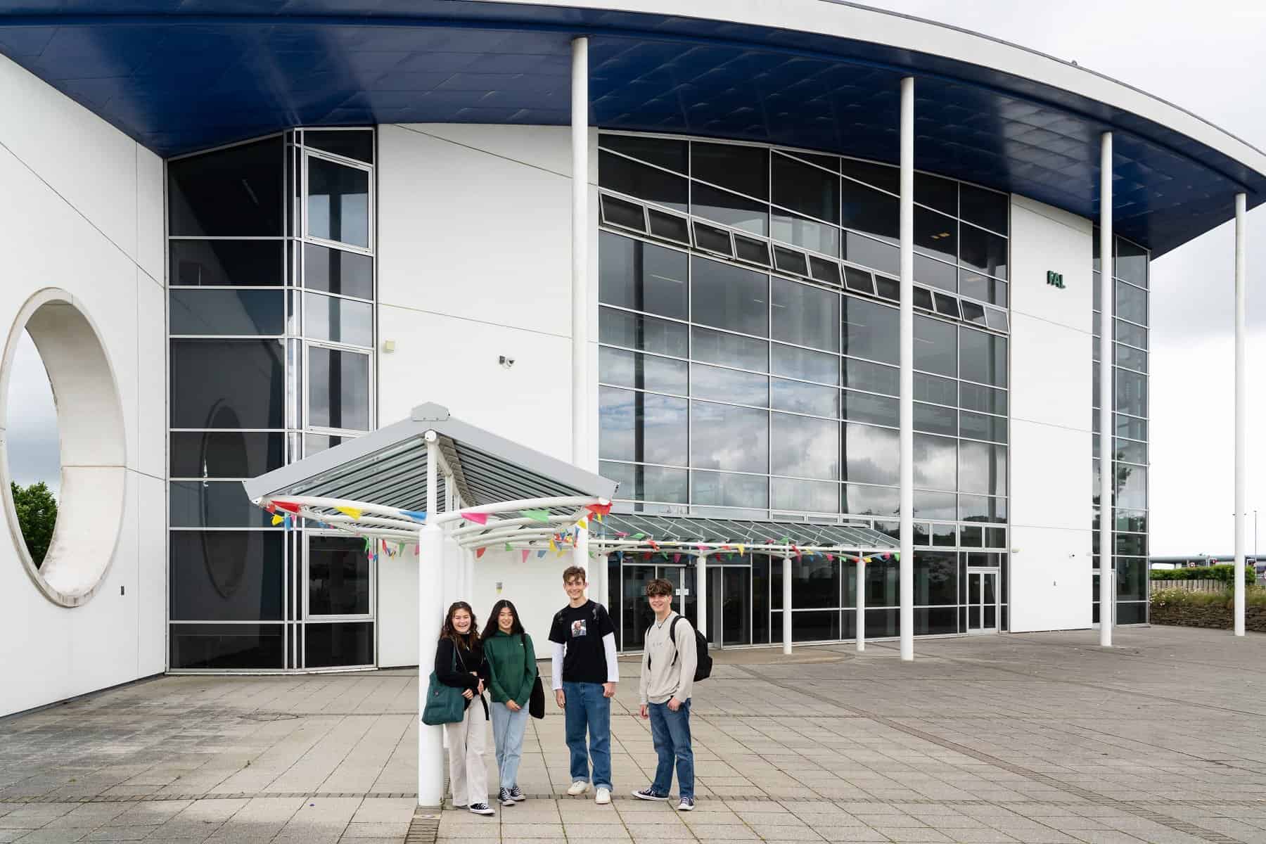 Four students stand outside of the Fal building. There is bunting on the pillars towards the entrance.