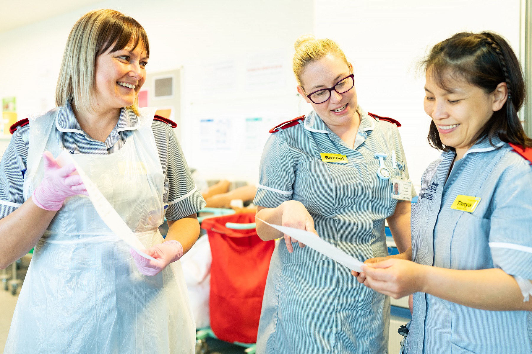 A trio of nursing students look at paperwork smiling all dressed in uniforms.