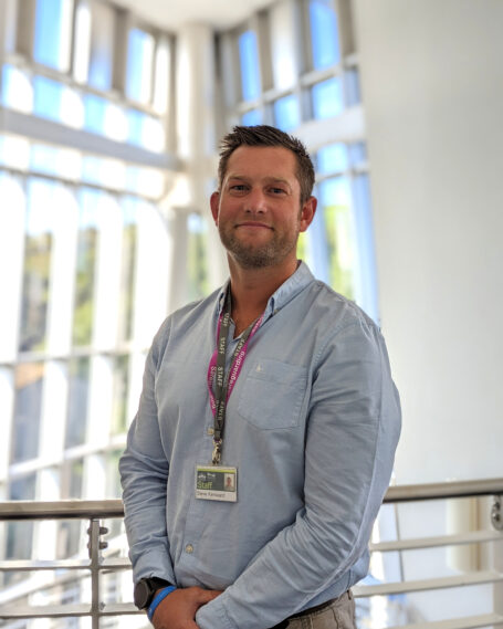 A portrait of Steve Kenward wearing a shirt and lanyard in front of large windows.