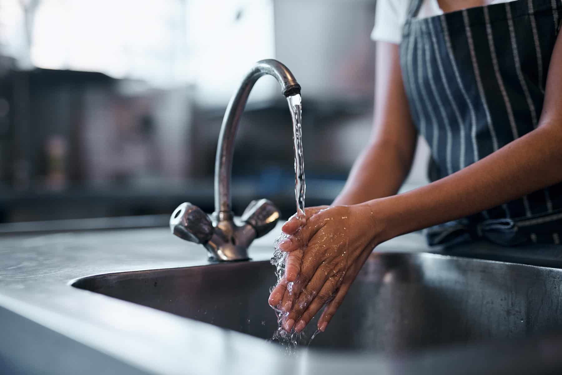 Cropped shot of a woman washing her hands in the sink of a commercial kitchen