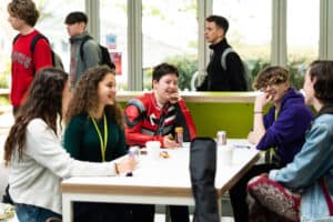 A group of students sit at a table in a canteen at Truro College. They all have drinks and are chatting.