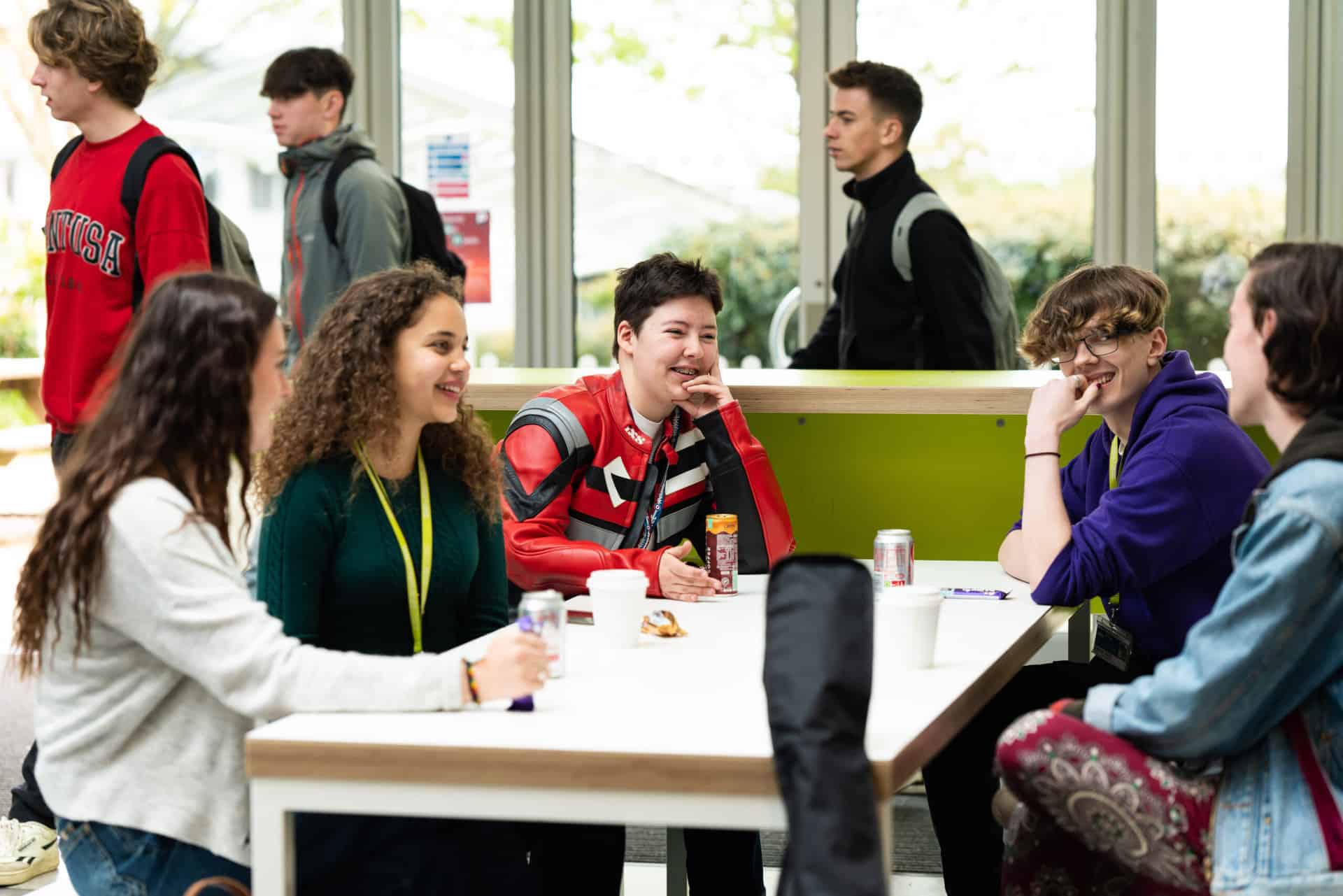 A group of students sit at a table in a canteen at Truro College. They all have drinks and are chatting.