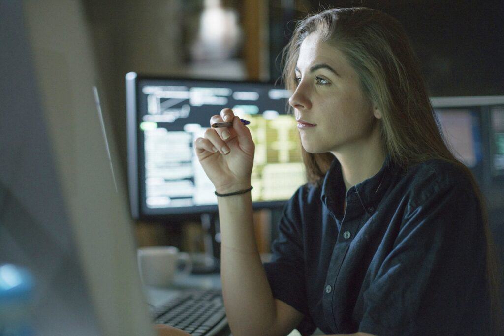 A young woman is seated at a desk surrounded by monitors.