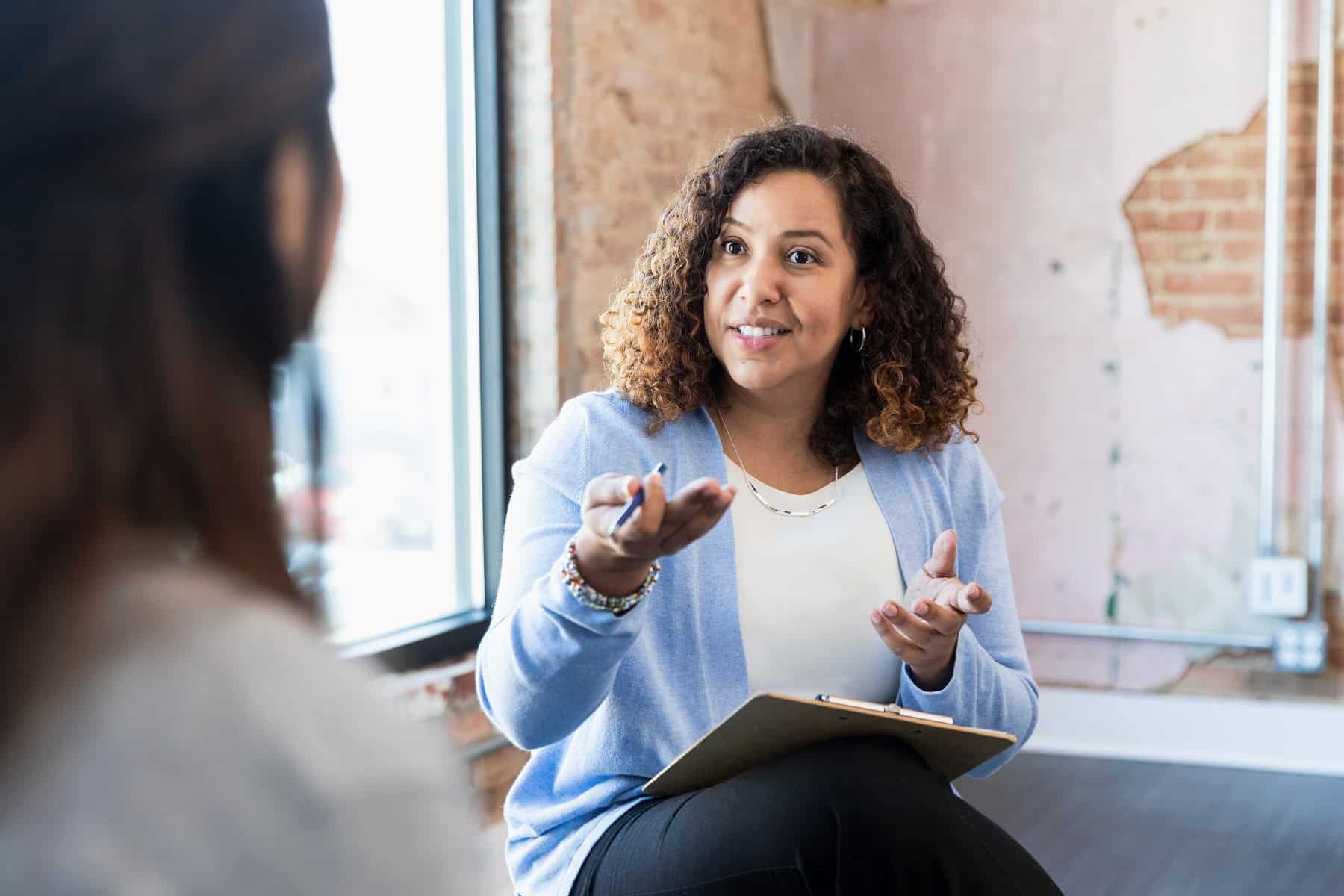 Meeting with someone one-on-one, the mid adult counselor gestures toward her unrecognizable female client.