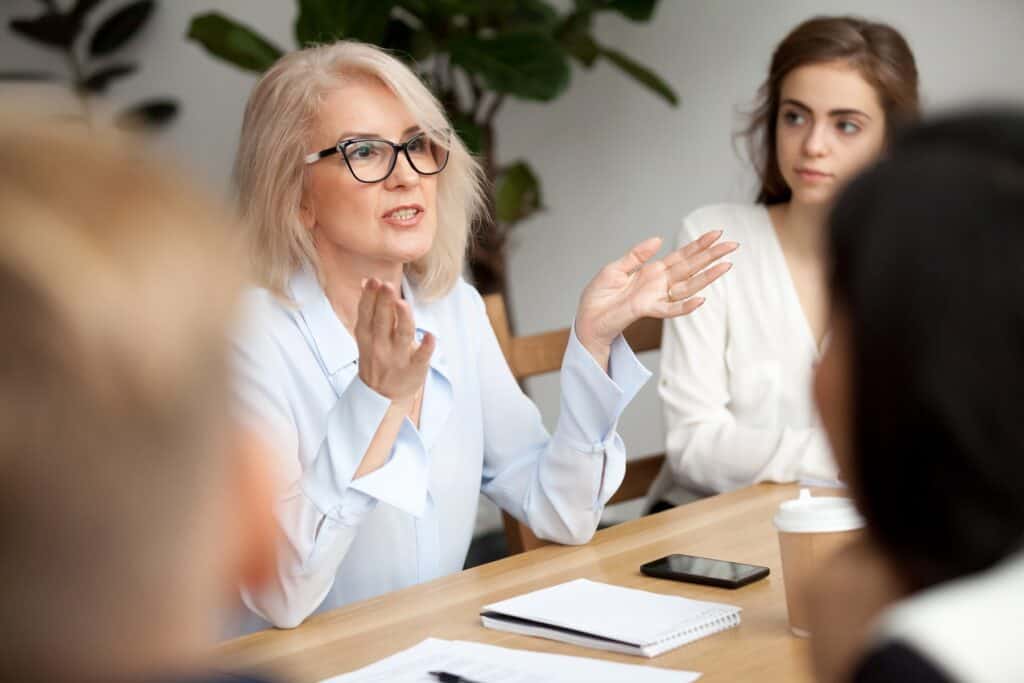 Businesswoman, teacher or mentor coach speaking to young people, senior woman in glasses teaching audience at training seminar, female business leader speaker talking at meeting