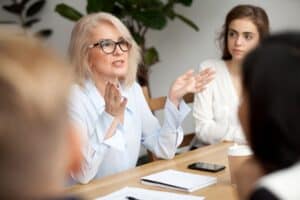 Businesswoman, teacher or mentor coach speaking to young people, senior woman in glasses teaching audience at training seminar, female business leader speaker talking at meeting