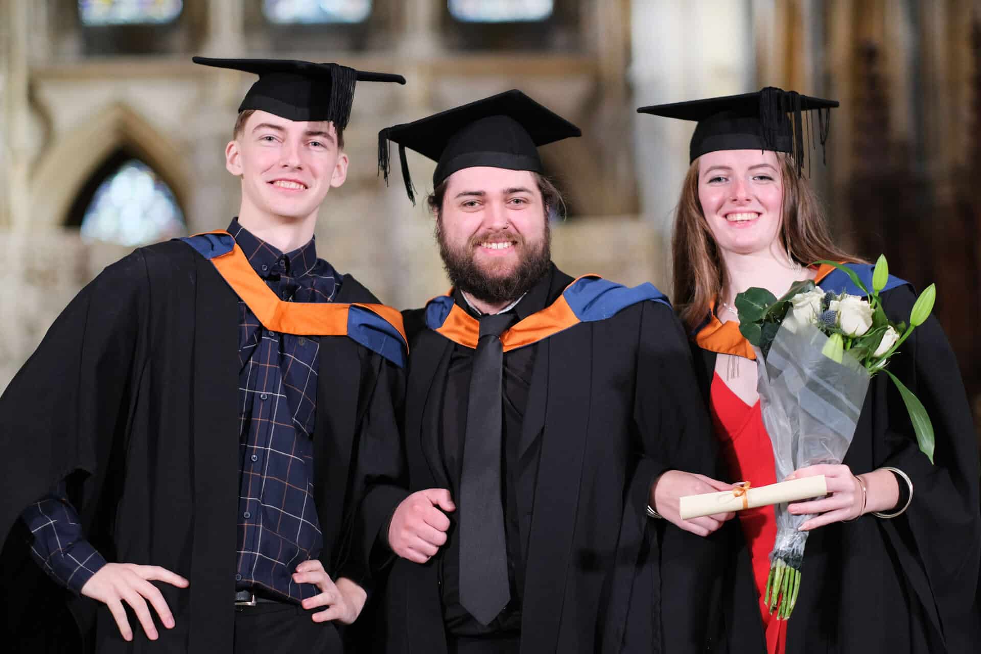 Graduate 23 The University Centre Truro & Penwith Graduation 2023. A trio of graduates linking arms and smiling at the camera.