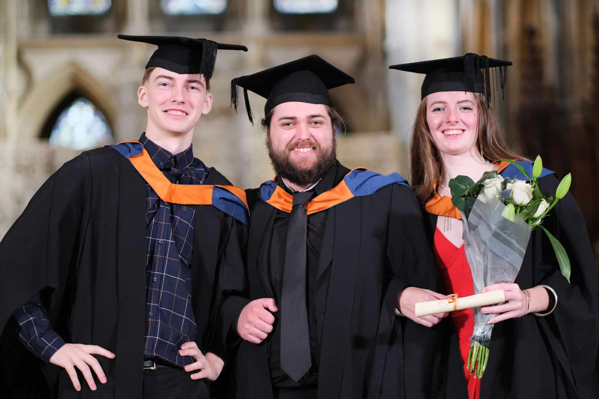 The University Centre Truro & Penwith Graduation 2023. A trio of graduates linking arms and smiling at the camera.