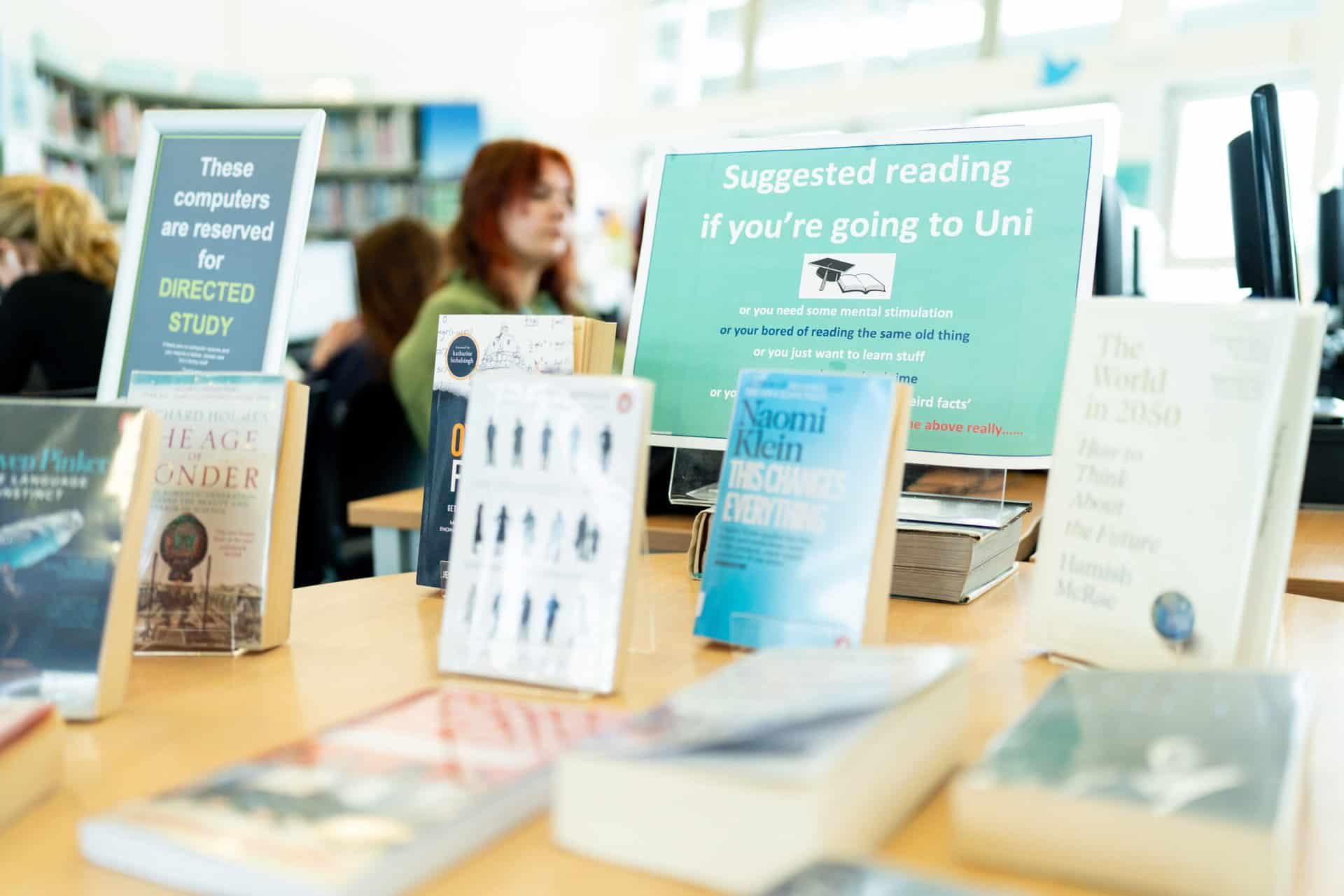 A display of books on a table in Penwith's Learning Centre. The sign on the display suggests that the books are good reads for those who are going to university. Students are studying in the background.