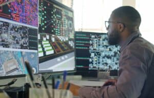 Image of a male designing electronic circuit boards. He’s sitting at a desk with a large computer screen displaying a variety of apps and illustrations.