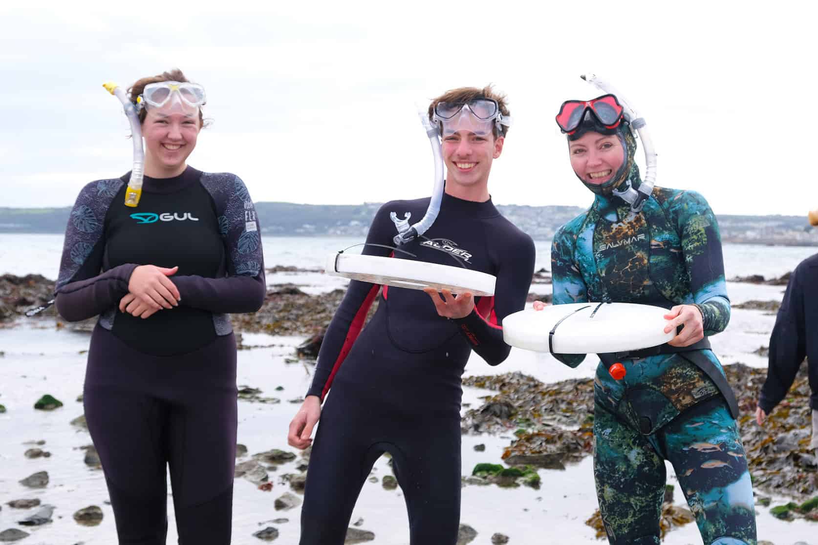 Staff and students of the marine academy in wetsuits at the beach releasing baby lobsters.