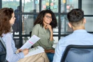 Happy young woman brainstorming marketing ideas about project strategy among coworkers, business startup creative team or students group in office holding papers.