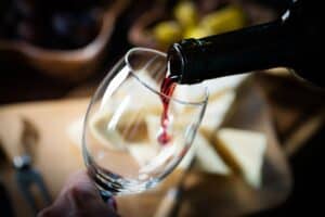 Pouring red wine into the glass in the background a table set with various types of cheese
