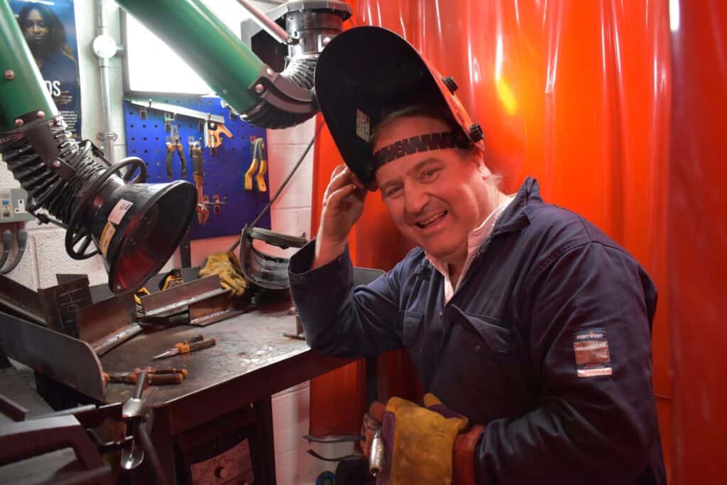 A photo of Andrew who completed a Welding bootcamp at Truro and Penwith College. He is lifting his welding mask and smiling.