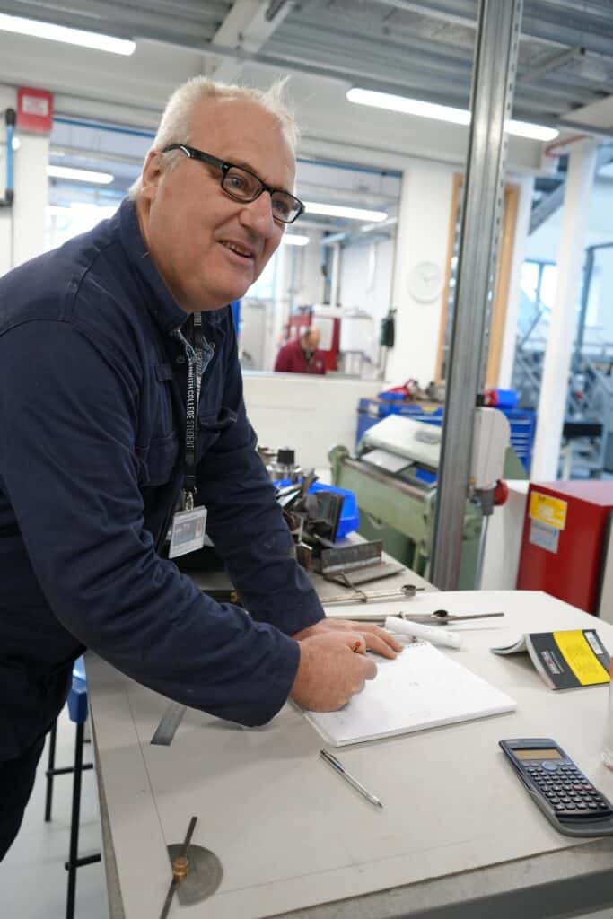 A photo of Andrew who completed a Welding bootcamp at Truro and Penwith College. He is using pencil and paper at a desk with other equipment on the table.