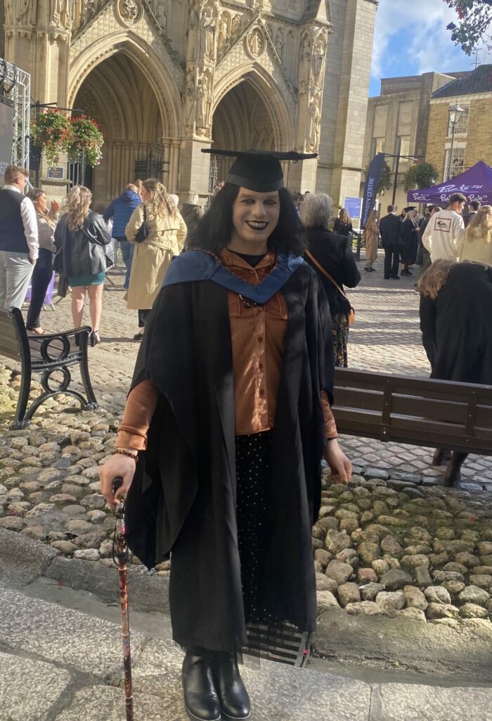 Student at standing outside Truro Cathedral wearing a graduation gown