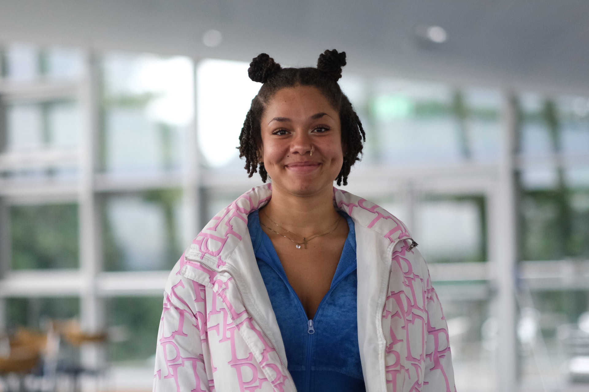 Anna Level 2 Certificate in Women's Hairdressing at Truro and Penwith College. Anna is wearing a pink and white jacket and is stood in a bright classroom, smiling at the camera.