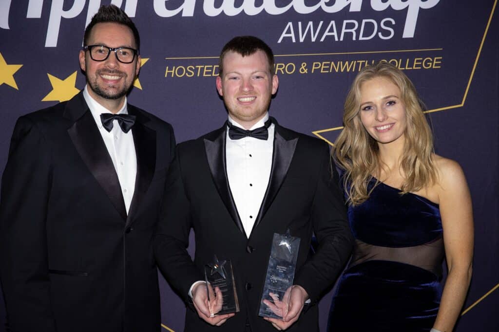 James Angliss stands in between Cornwall Apprenticeship Award presenters Holly Day and Neil Caddy with a glass trophy in each hand wearing a dinner jacket and bow tie.