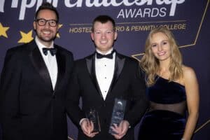 James Angliss stands in between Cornwall Apprenticeship Award presenters Holly Day and Neil Caddy with a glass trophy in each hand wearing a dinner jacket and bow tie.