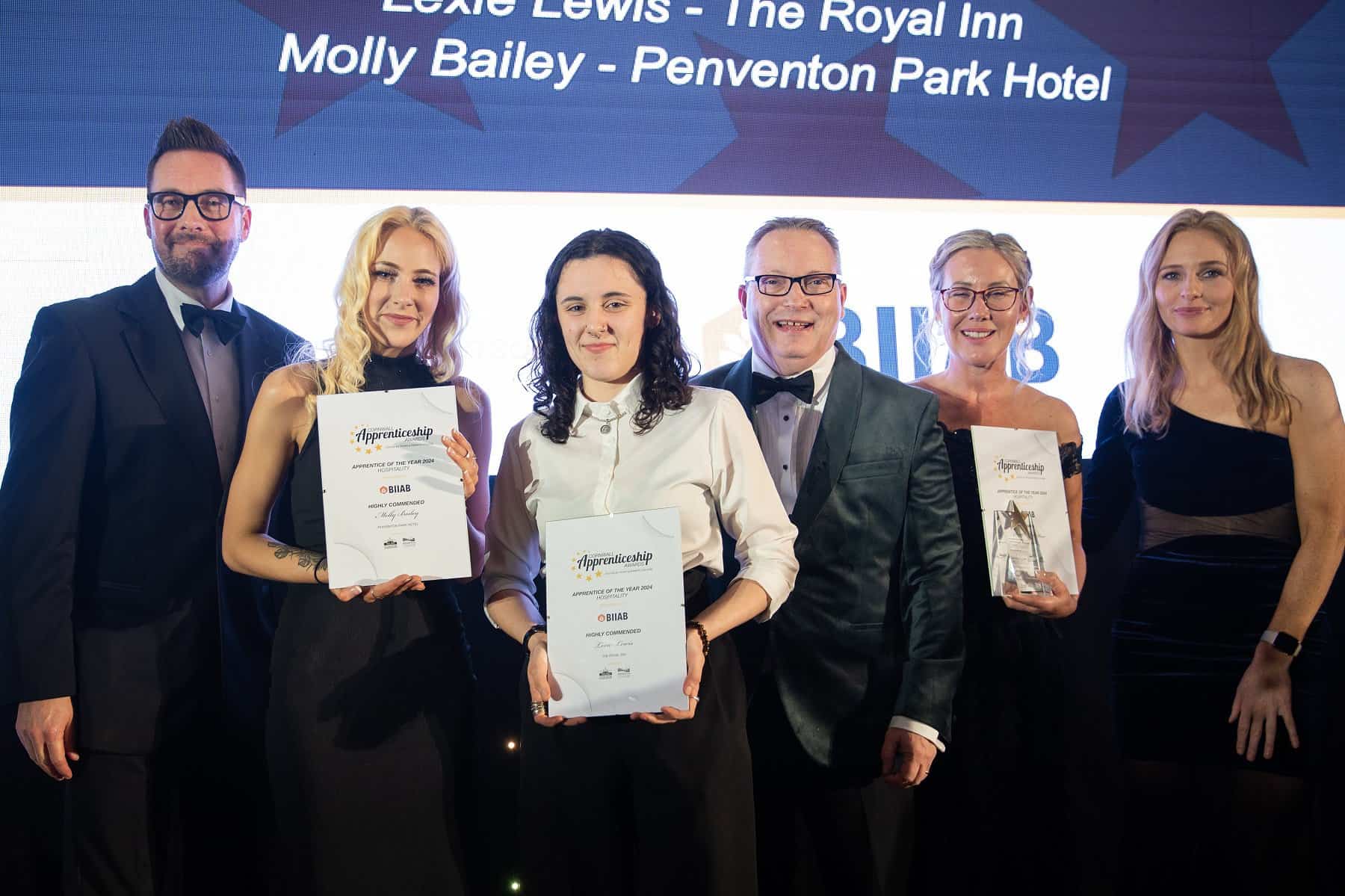 An image from the Cornwall Apprenticeship Awards 2024. Three winners stand with the hosts on the stage in formal wear.