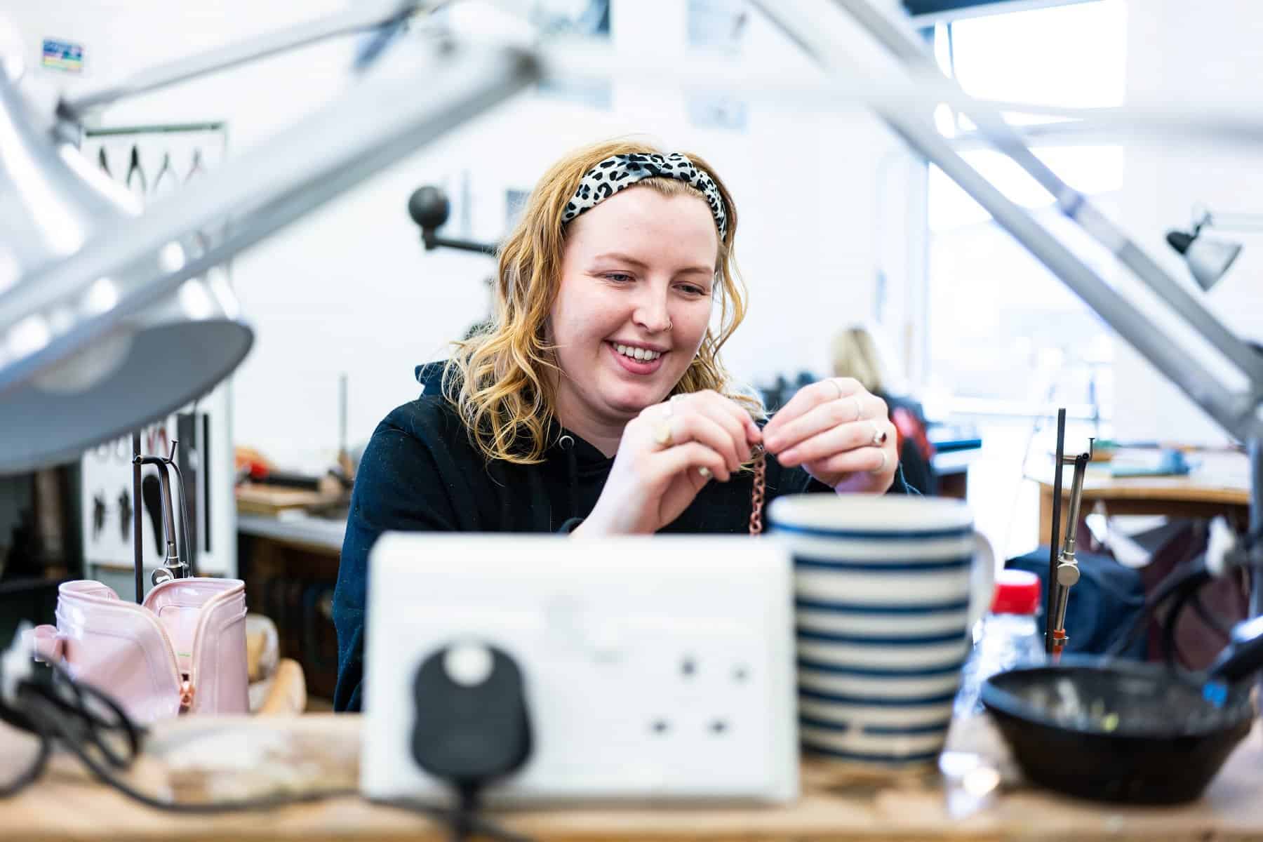 An art student looks closely at a piece of jewellery within an artists studio.