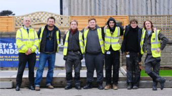 A group of men in hi vis jackets stand smiling together in front of their finished project.