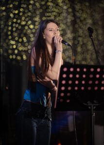 A female music student sings into her microphone on stage during the event reception