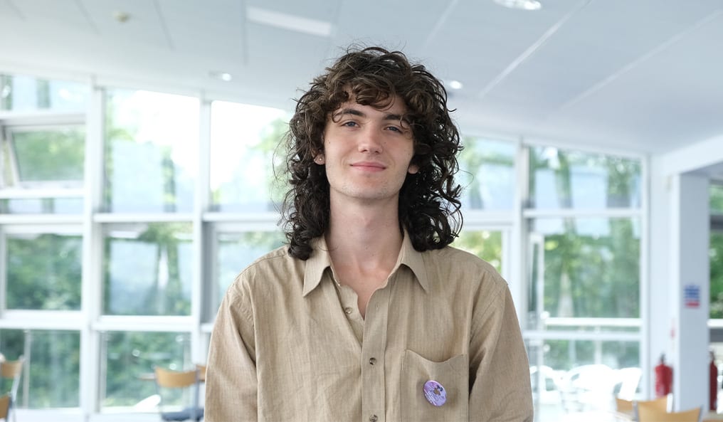 A young man in a beige button up shirt smiles for the camera.