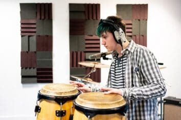 A student has headphones on and is playing a drum set with their hands.