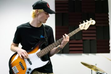 A student plays an electric guitar looking at his hand.