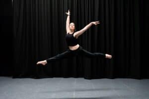 A performing arts dance student leaps into the air on a stage with a dark backdrop.